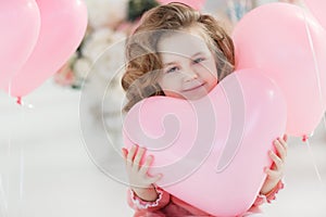 Beautiful preschool girl in a white studio with pink heart-shaped balloons