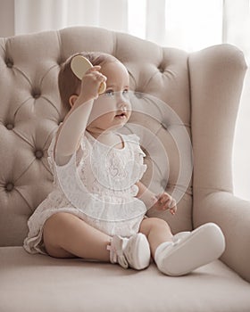 Beautiful pretty little baby girl sitting on the chair and holding hair comb