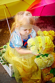 A beautiful pretty little girl looking like a doll in a beautiful dress with yellow umbrella in nature on a summer day