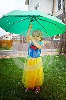 A beautiful pretty little girl looking like a doll in a beautiful dress with yellow umbrella in nature on a summer day