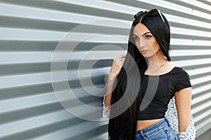 Beautiful pretty modern young brunette woman with long hair in vintage jeans in a stylish black top in a summer jacket resting