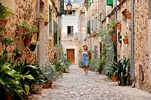 Beautiful pretty woman walking at old town pavement street with flowers and looking away. Travel concept