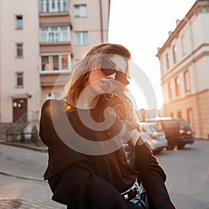 Beautiful pretty young hipster woman in trendy clothes in retro style in fashionable dark sunglasses is posing outdoors
