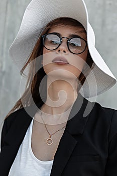 Beautiful pretty young woman with beauty lips in elegant glasses in sexy top in fashion black blazer and summer straw hat near