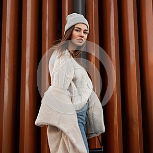 Beautiful pretty young woman in a stylish knitted sweater in a fashionable warm hat with a youth coat of their faux fur posing