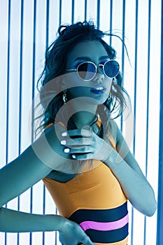 Beautiful pretty young woman is sunbathing in a solarium. Sexy glamorous girl model in stylish sunglasses with a curly hairstyle