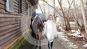 Beautiful professional female jockey walking with brown horse on farm. Friendship with horse