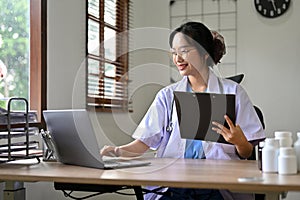 Beautiful Asian female doctor using laptop computer, working at her desk in the doctor`s office