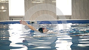 Beautiful professional swimmer swiming backstroke in the pool, camera dolly shot