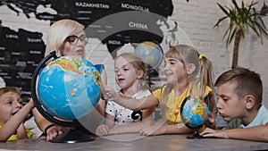 Beautiful pupils and teacher looks at globes in geography classroom on the lesson at the elementary school. Boys, girls
