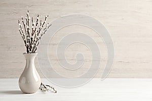 Beautiful pussy willow branches in vase on white wooden table, space for text