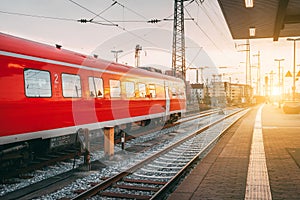 Beautiful railway station with modern red commuter train at sunset