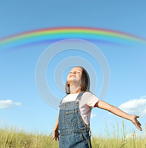 Beautiful rainbow in blue sky over cute little girl in field on sunny day