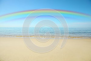 Beautiful rainbow in blue sky over sandy beach and sea on sunny day