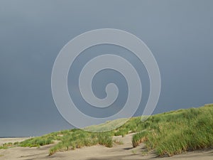 Beautiful rainbow in gray sky over sandy and grassy beach in North Sea. on Juist island in Germany