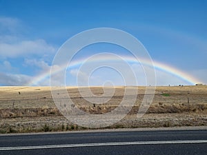 Beautiful rainbow over a golden field captured from side road