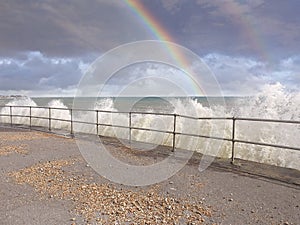 Beautiful rainbow sky and stormy waves crashing on wall