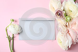 Beautiful ranunculus flowers and envelope on color background, top view.