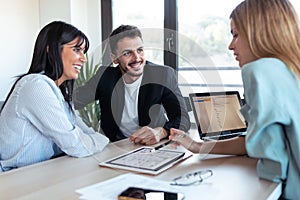 Beautiful real-estate agent showing house plans on electronic tablet while talking to the couple about buying the house in the