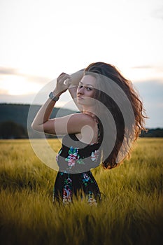 Beautiful realistic smile of brunette in black dress standing in the middle of a field during sunset. Candid portrait of inner