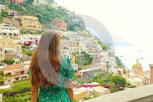 Beautiful rear view of a romantic sweet woman in green dress looking at Positano village from a terrace, Amalfi Coast, Italy