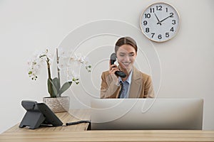 Beautiful receptionist talking on phone at counter in hotel