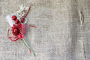 A beautiful red artificial flower with a green stem on the texture of a brown old linen cloth, linen natural material with a rough