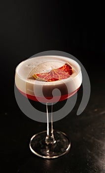 Beautiful red cocktail with white froth decorated with mint in a glass chalet isolated against a black background. close