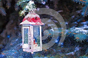 Beautiful red fairytale lantern hanging on snowy fir branch in forest