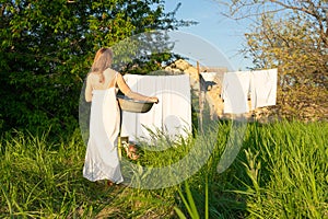 beautiful red girl in nightie hanging laundry outdoors. village woman working in countryside.