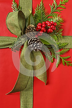 Beautiful red and green Christmas gift present with fabric ribbon bow and botanical decorations. Vertical background image.