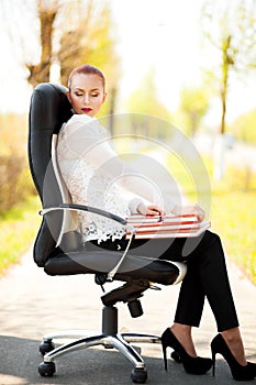 Beautiful red-hair business lady sitting on office chair with books