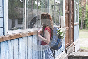 Beautiful red hair woman with backpack looking in the window of scary old house