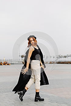 Beautiful red-haired girl in a black coat and a beret walks through the city