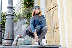 Beautiful red-haired girl in a blue sweater and hat walks around the city