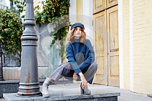 Beautiful red-haired girl in a blue sweater and hat walks around the city