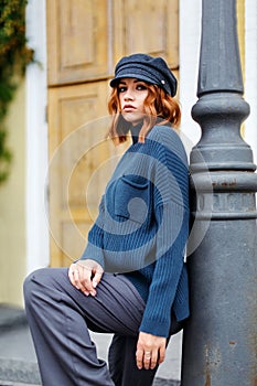 Beautiful red-haired girl in a blue sweater and hat walks around the city