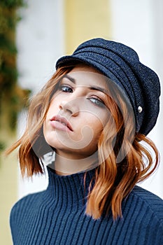Beautiful red-haired girl in a blue sweater and hat walks around the city
