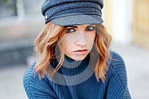 Beautiful red-haired girl in a blue sweater and hat walks around the city