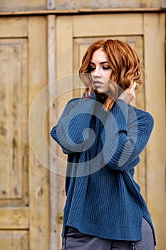 Beautiful red-haired girl in a blue sweater and hat walks around the city