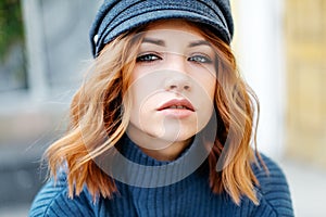 Beautiful red-haired girl in a blue sweater and hat walks around the city