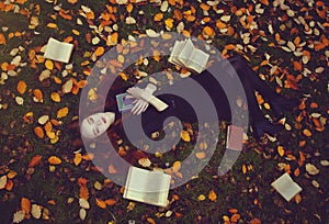 Beautiful red-haired girl with books lies on the grass in an autumn forest, top view. Autumn Fairytale photoshoot.
