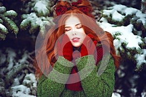 Beautiful red haired girl with creative hairstyle posing with closed eyes in front of snow covered firtrees photo