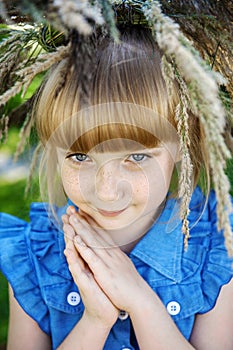 Beautiful red-haired girl with freckles and a wreath of summer herbs on her head looks into the camera with blue eyes. Young