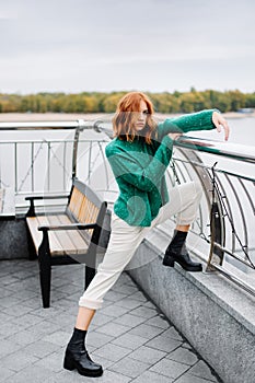 Beautiful red-haired girl in a green sweater walk on the street