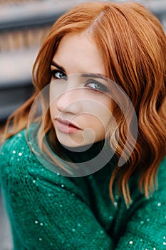 Beautiful red-haired girl in a green sweater walk on the street