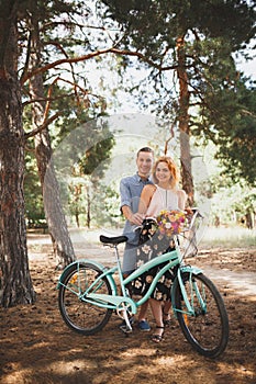 Beautiful red-haired girl with a guy standing in a forest holding flowers in hands.