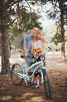 Beautiful red-haired girl with a guy standing in a forest holding flowers in hands.