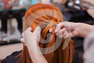 Beautiful red-haired girl, hairdresser weave a French braid close-up