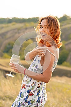 Beautiful red-haired girl is having fun and dancing in a field at sunset